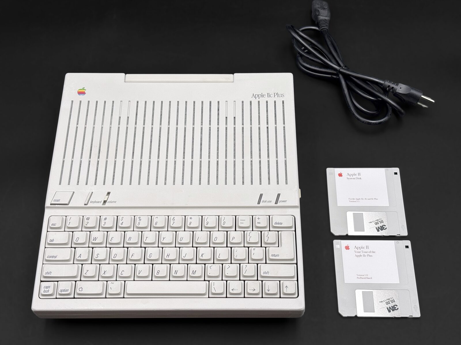 Apple IIc Plus with its power cord and two 3.5-inch Apple II system disks